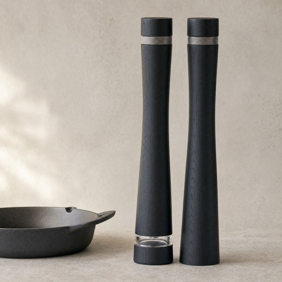 Two tall black ash column mills standing beside a cast iron pan, seen from a low angle